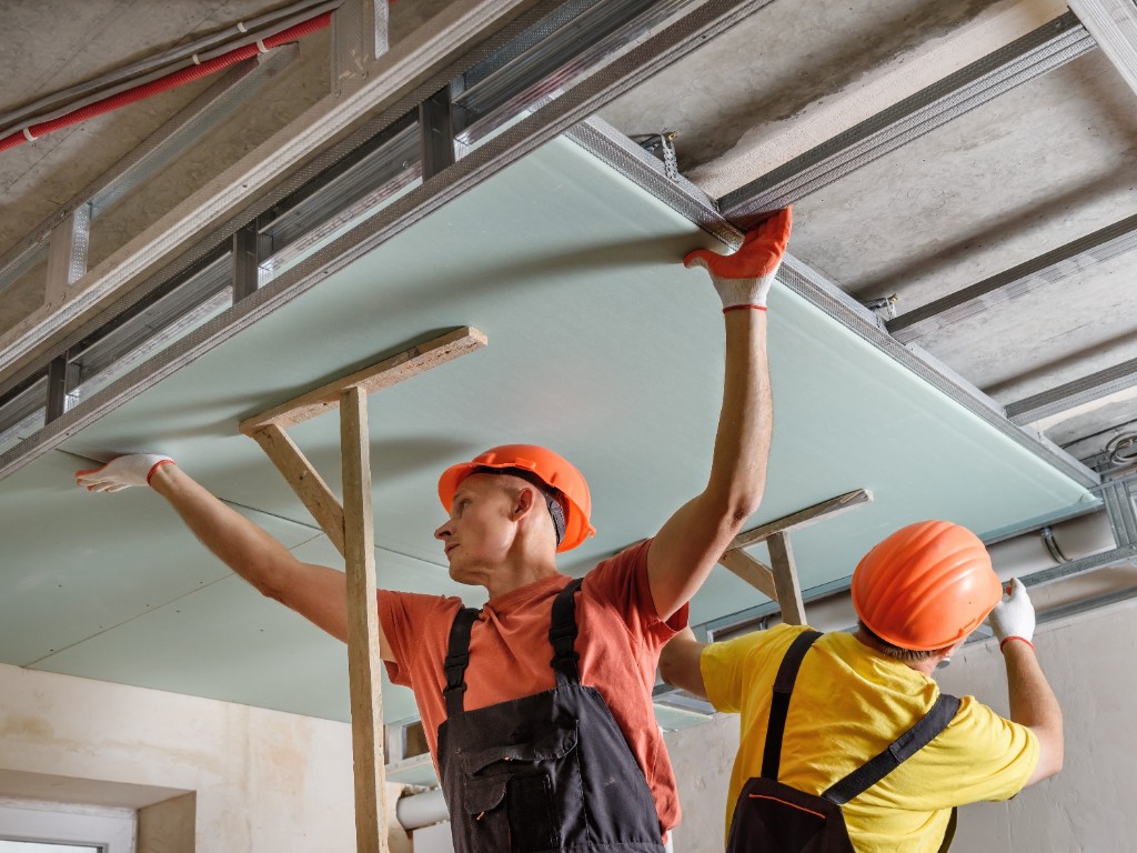 Trockenbau: Zwei Fachkräfte montieren eine Gipskartonplatte an der Deckenkonstruktion